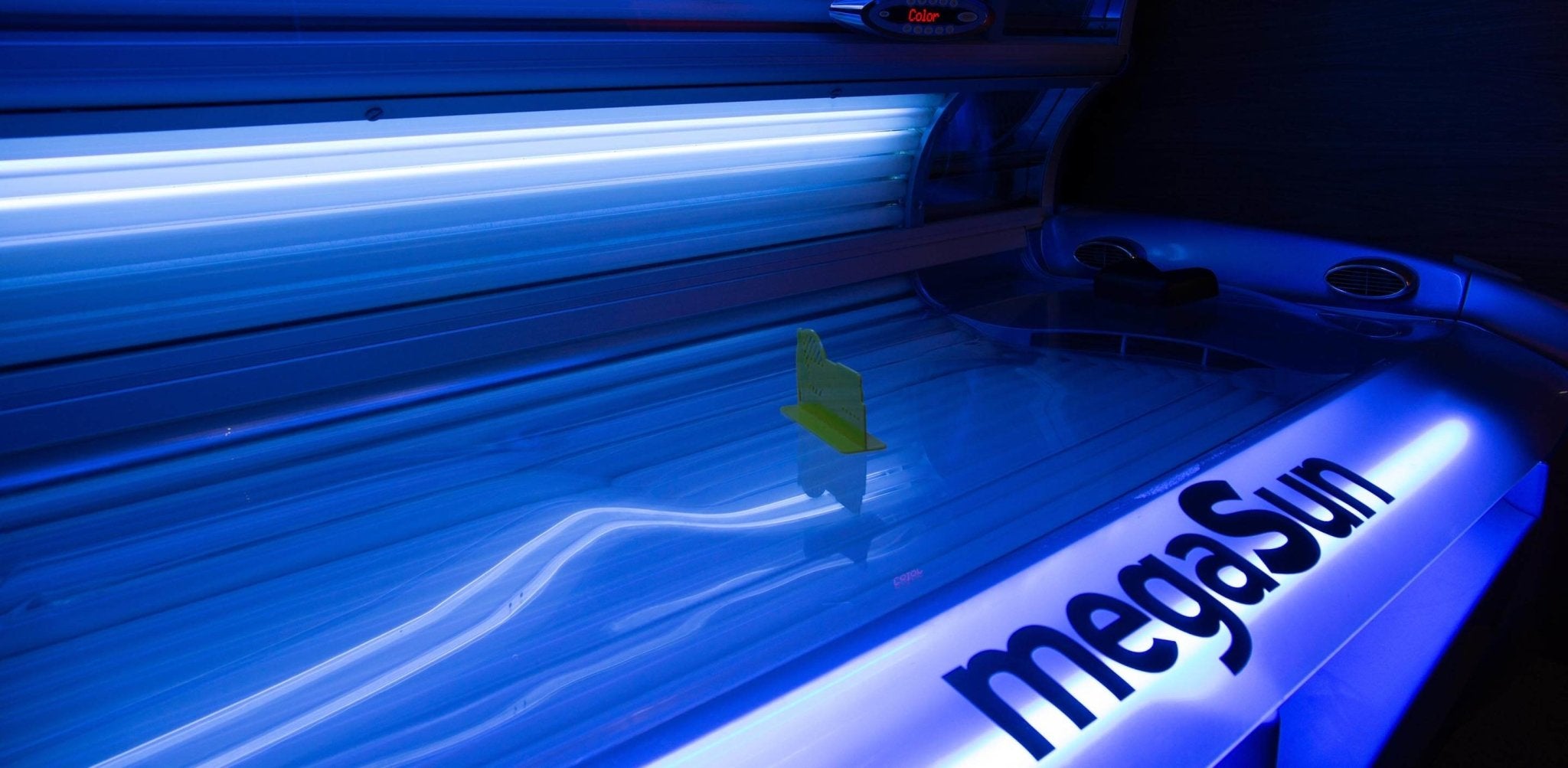 A small object sits illuminated inside a bright blue tanning bed with glowing tubes.