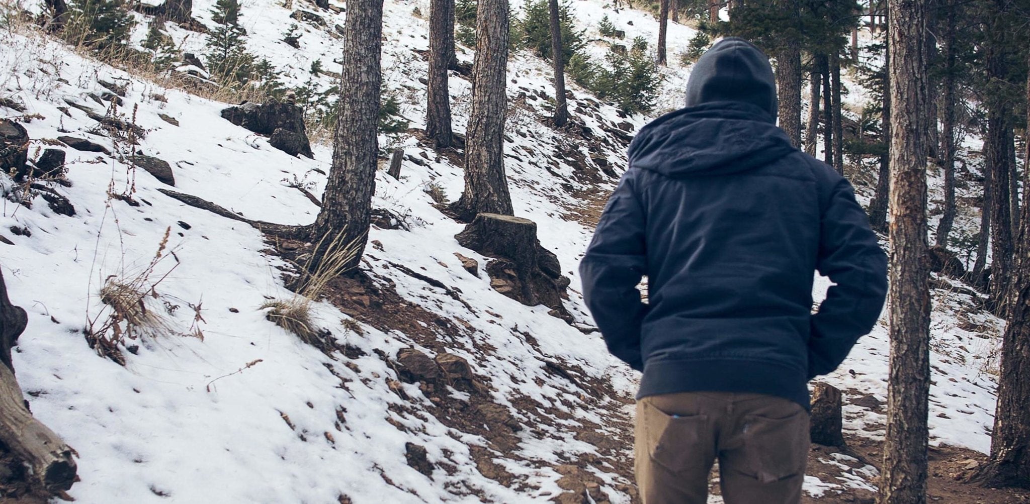 Man in dark jacket standing on snowy forest slope during winter.