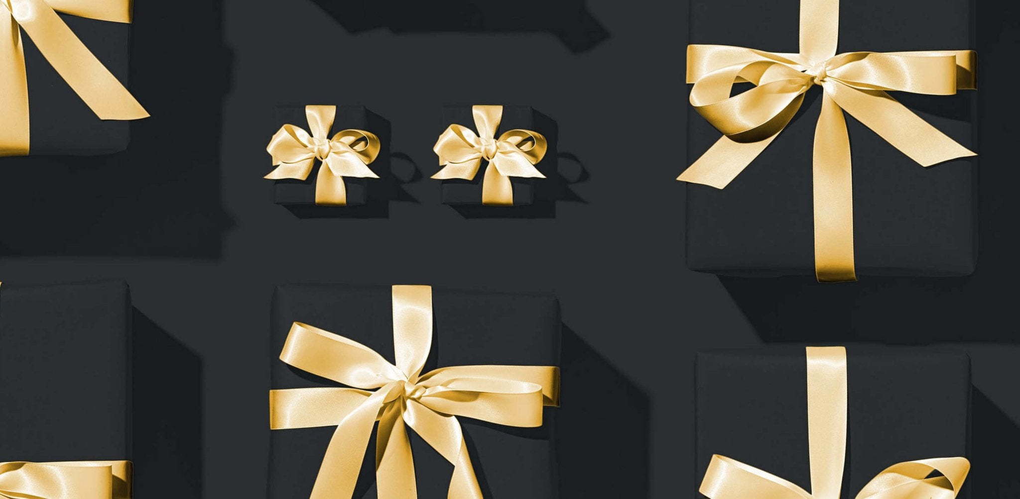 Black gift boxes with gold ribbons arranged on dark background, suggesting self-tanning products as presents.