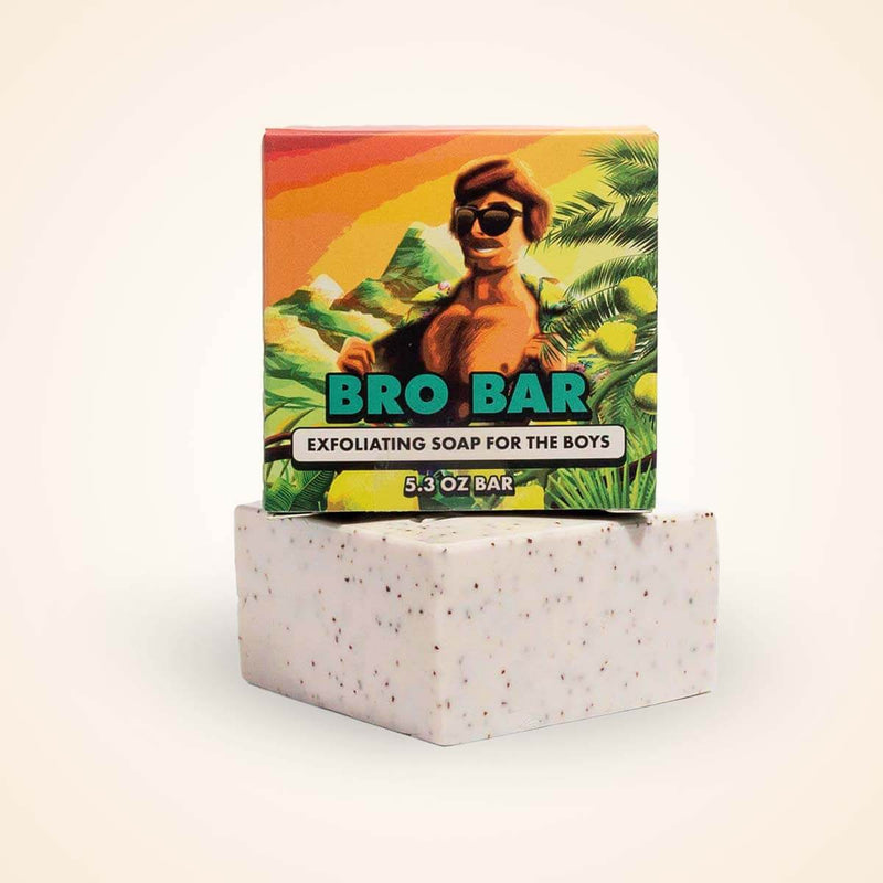 A tropical-themed soap bar with speckled white texture sits beneath its colorful packaging featuring a man in sunglasses.