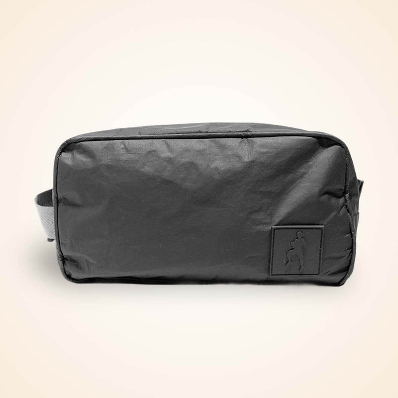Black nylon toiletry bag with carry handles and small front pocket against cream background.