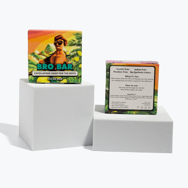 Tropical-themed exfoliating soap bars displayed on white cubes, showing colorful front and back packaging.