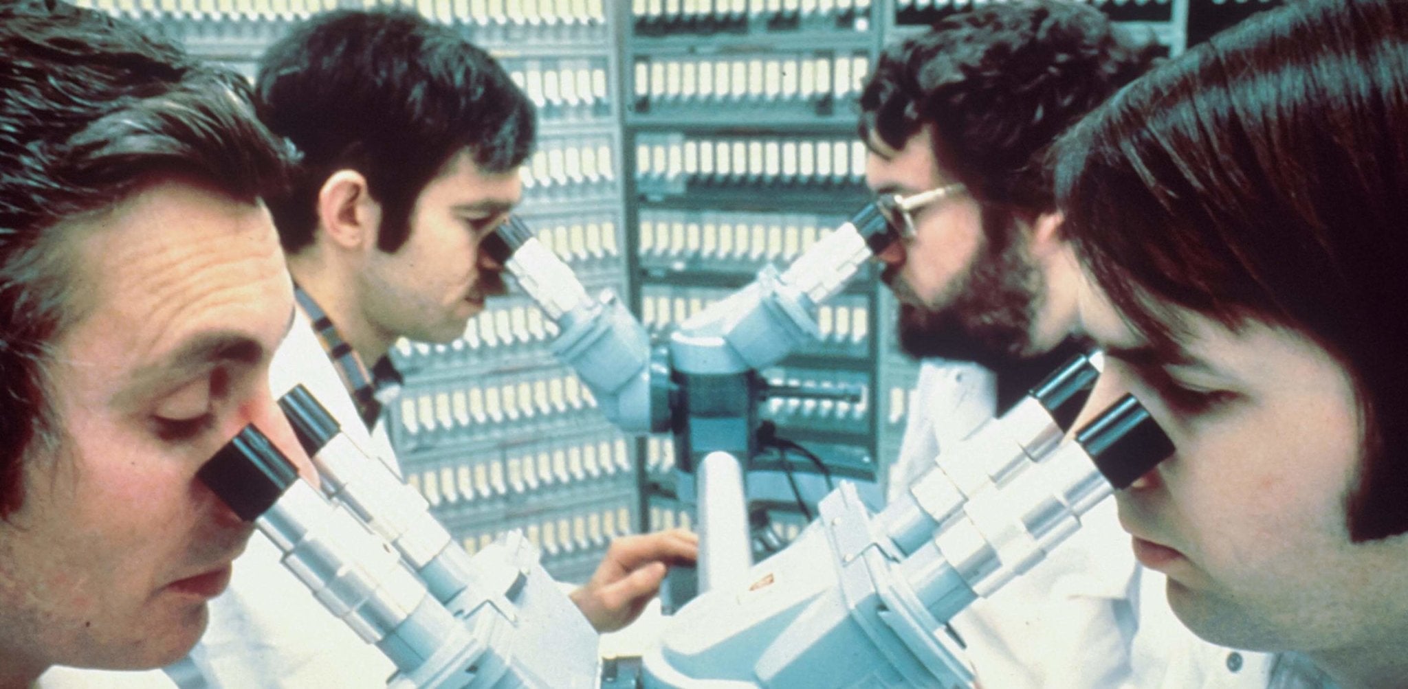 Four scientists in white lab coats examine test tubes in a vintage laboratory setting.