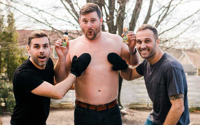Three men outdoors holding spray tan bottles, celebrating with playful poses and expressions.