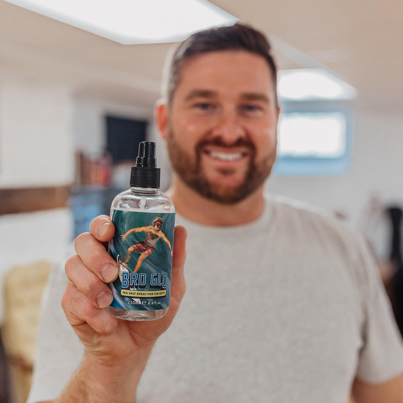 Man holding a spray bottle of clear liquid with a sports-themed label in a bright kitchen.