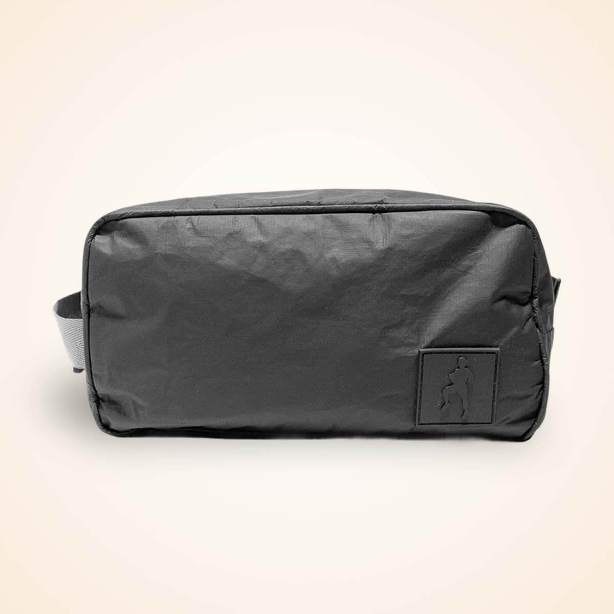 Black nylon toiletry bag with carry handles and small front pocket against cream background.