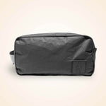 Black nylon toiletry bag with carry handles and small front pocket against cream background.