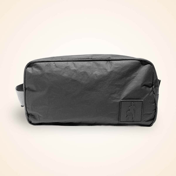 Black nylon toiletry bag with carry handles and small front pocket against cream background.