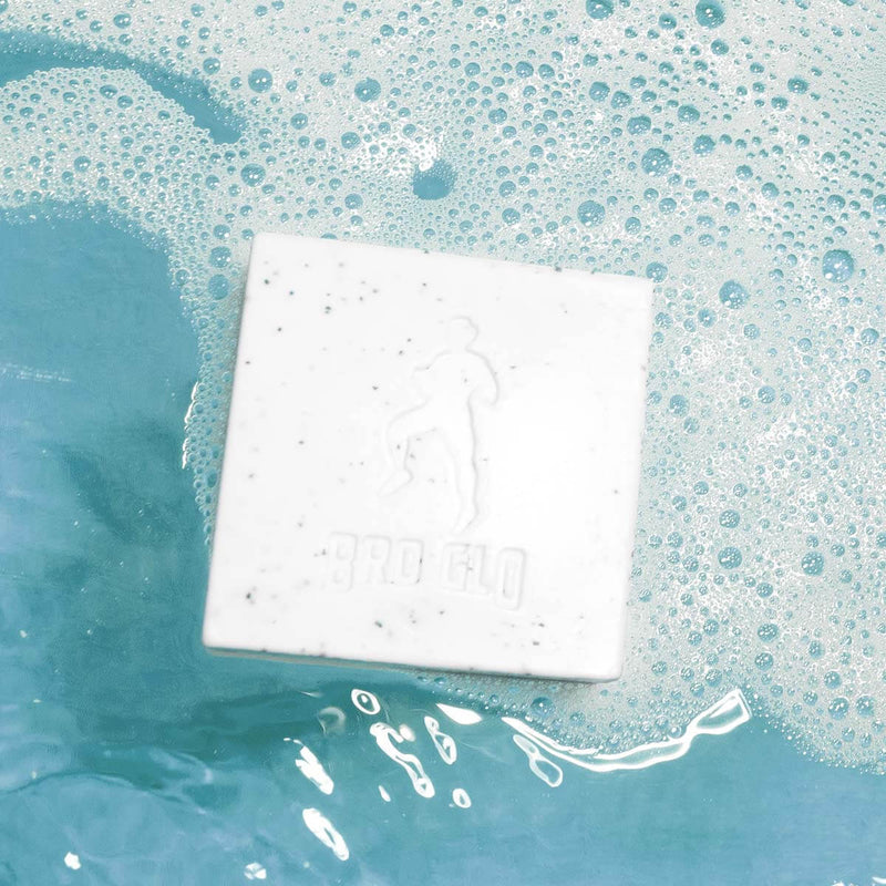 White exfoliating soap bar with embossed design soaking in turquoise soapy water with bubbles.